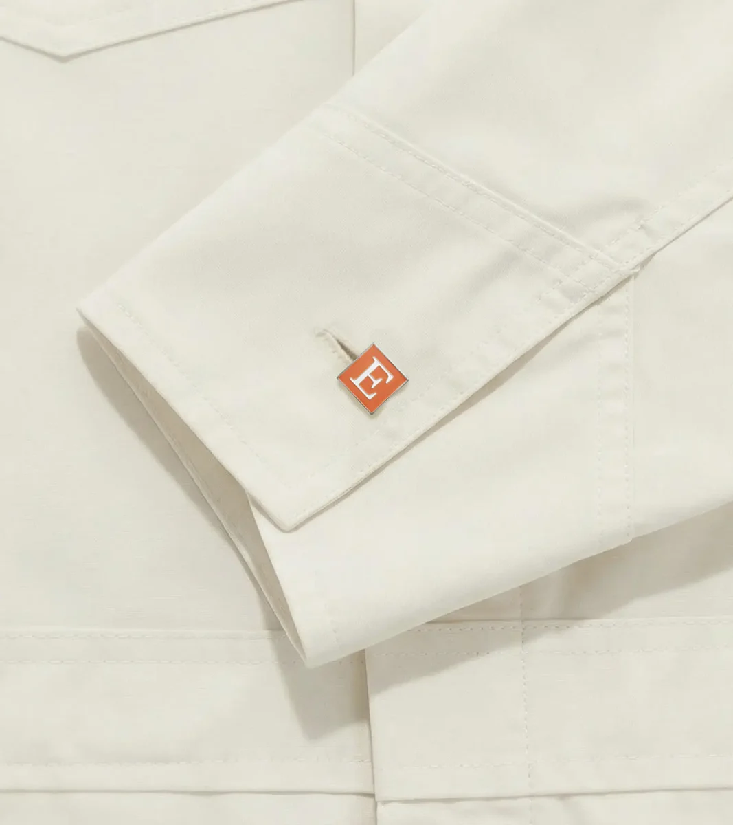 Puño de camisa color crema con una pequeña etiqueta naranja de Etsy