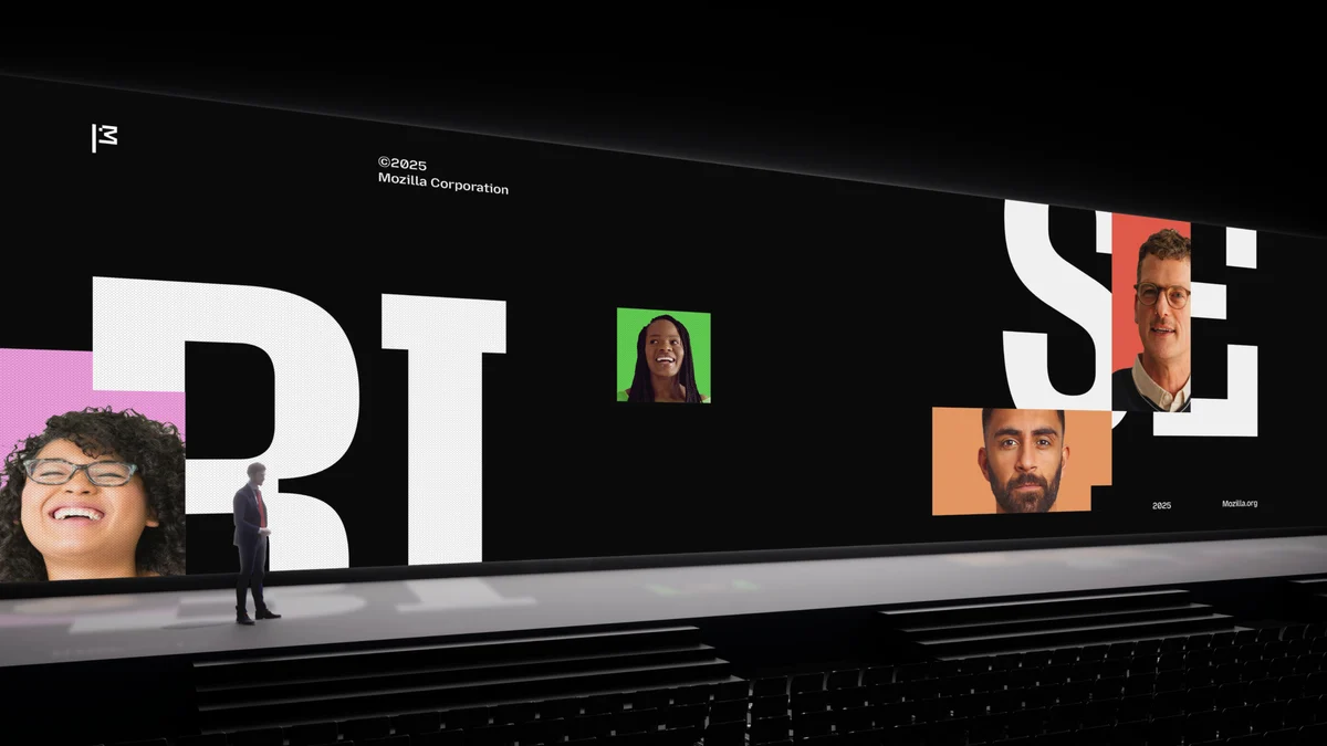 Una gran presentación en el escenario con un fondo negro llamativo que muestra tipografía blanca de gran tamaño y retratos vibrantes de diversas personas sobre bloques de colores. El logo de la bandera de Mozilla aparece en la parte superior izquierda, con «©2025 Mozilla Corporation» a la derecha. Un presentador está en el escenario, enfatizando una estética de diseño moderna, inclusiva e impactante.