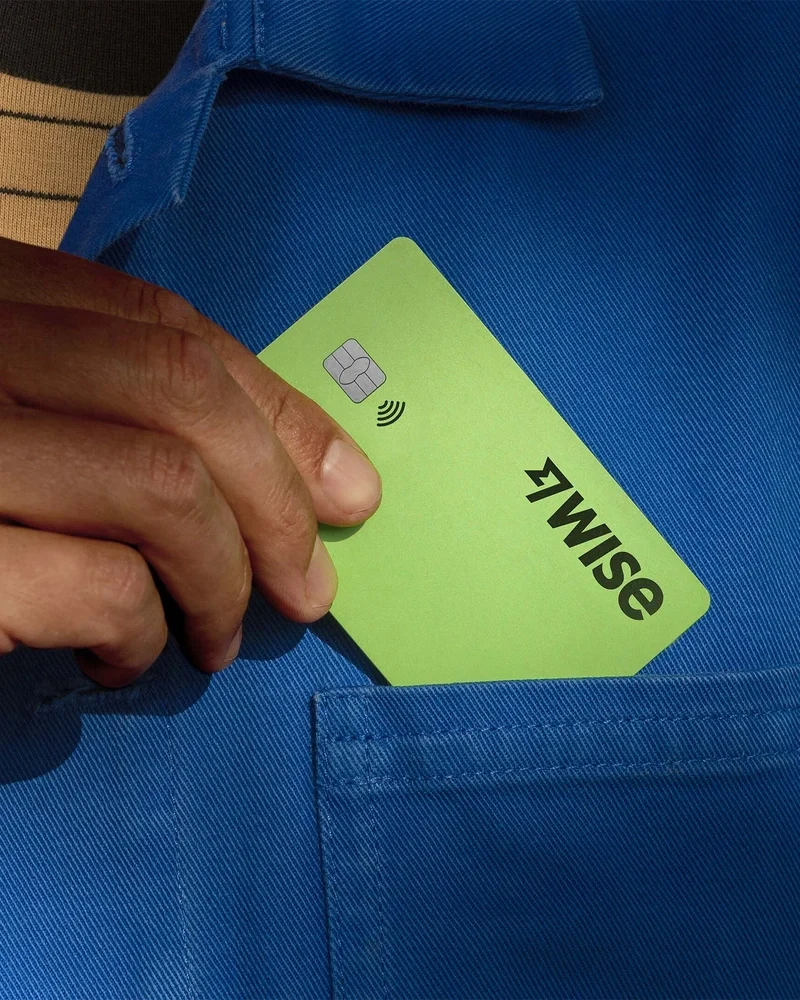 Mano sacando una tarjeta verde brillante de Wise de un bolsillo